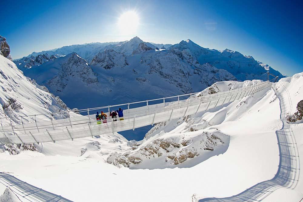 Vier Wintersportler genießen die Aussicht auf der Hängebrücke Cliffwalk in Titlis